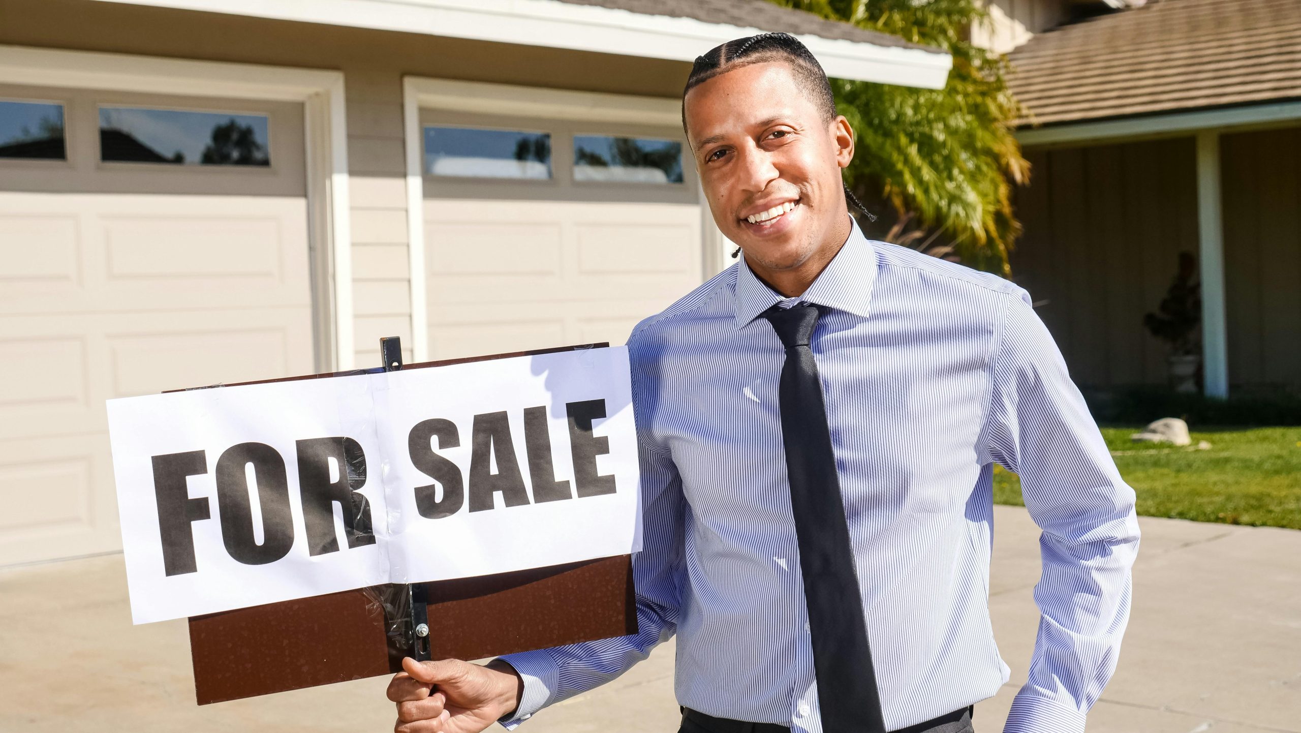 Realtor holding a for sale sign smiling at the camera