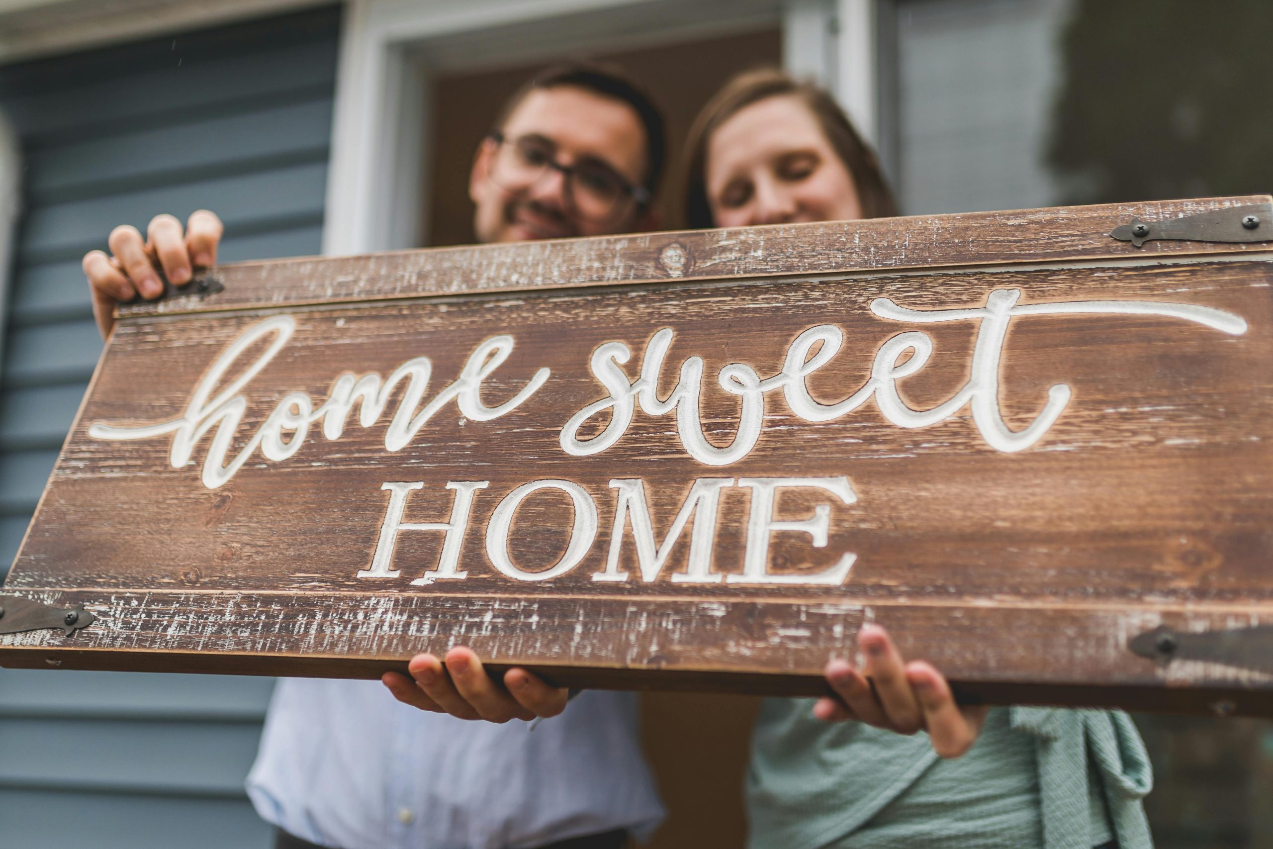 Happy first time home buyers holding a sign that reads "Home sweet home"
